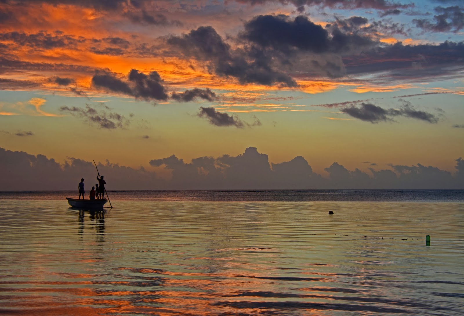 Fishermen on a small boat at sunset over the calm Mauritian lagoon